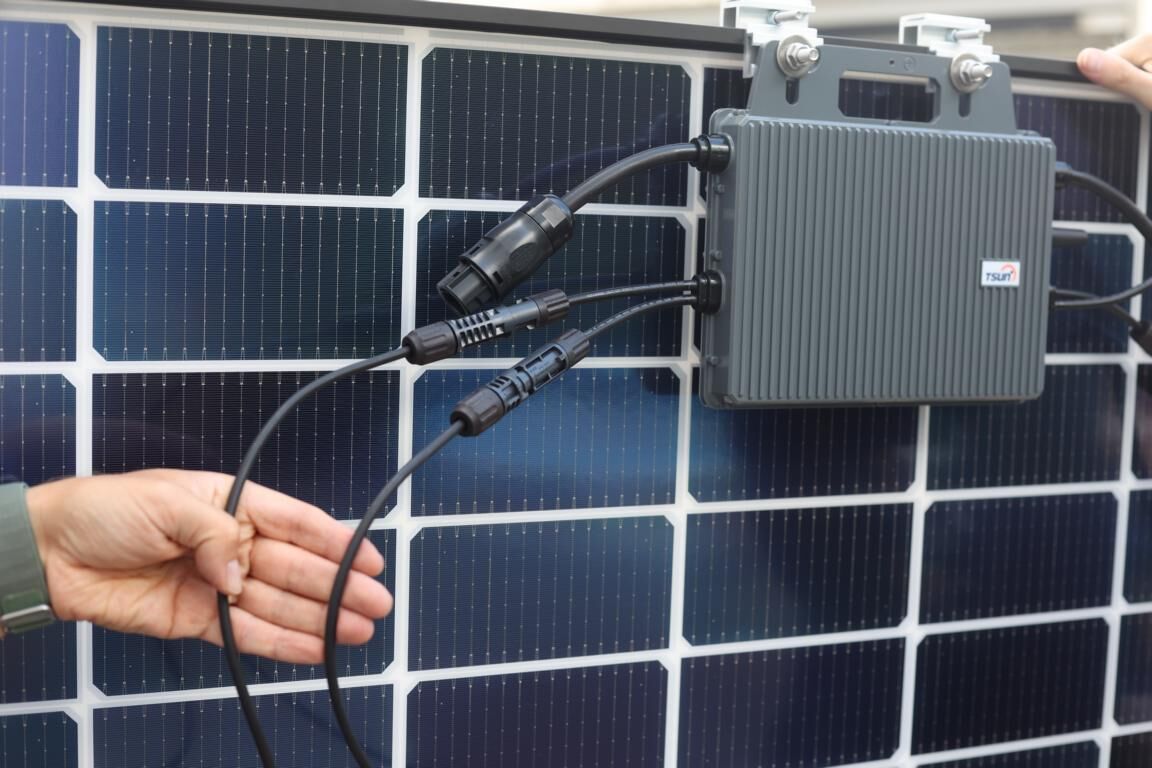 Ein Wechselrichter ist an den Rahmen eines Solarmoduls befestigt und er wird im Balkonkraftwerk Test mit dem Solarmodul verkabelt.